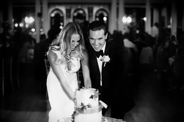 A black and white photo of a groom and bride cutting their wedding cake