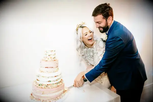 A bride and groom laugh as they cut their wedding cake