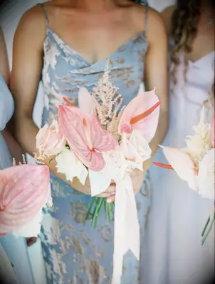 bridesmaids in mismatched blue and purple dresses holding pink bouquets with anthurium, roses and astilbe