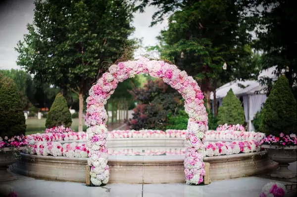 outdoor wedding ceremony with floral arch made of pink and white hydrangeas and roses in front of stone fountain 