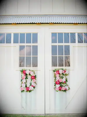 wedding venue with white barn doors decorated with the letters D and E made from pink flowers