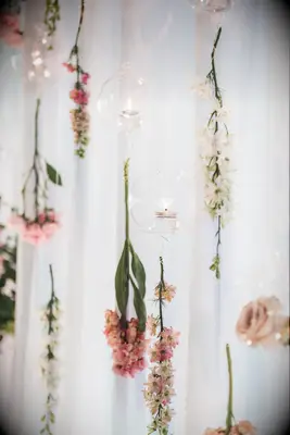 pink and white flowers hanging from clear fishing line against a white curtain backdrop with votive candles in floating glass orbs