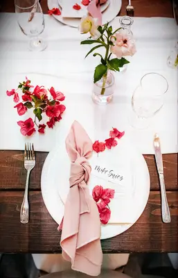 aerial view of wedding place setting with pink cloth napkin, white charger plate and pink bougainvillea flowers on the plate