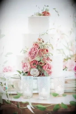 three tier white buttercream wedding cake decorated with pink flowers and greenery