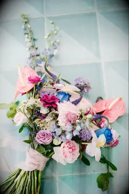pink and purple wedding bouquet with anthurium, roses, and delphinium laid on the floor against a blue tile backdrop