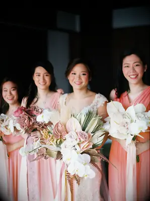bride and bridesmaids holding modern wedding bouquets with anthurium, pink roses, white orchids and dried fan palms