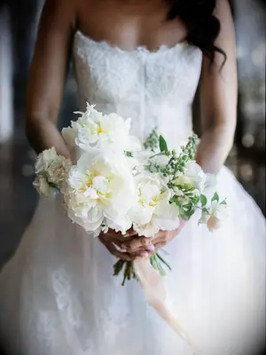 A bride holds a vibrant white peony bouquet.