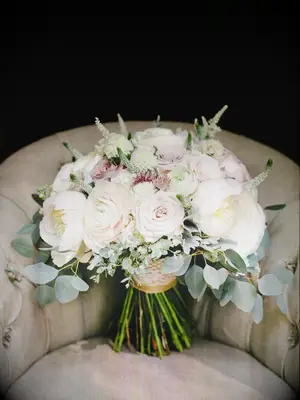 A cream-colored chair holds an overflowing white peony and rose bouquet.