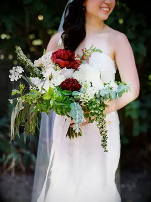 A bride holds an overflowing bouquet of white and red peonies.