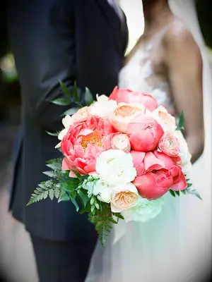 A couple stand together holding a white rose and vibrant pink peony bouquet.