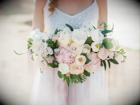 A bride holds a stunning bouquet of white roses and pale pink peonies.
