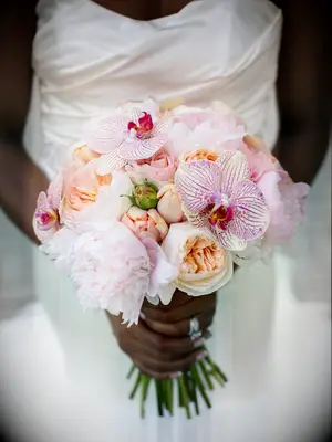 A bride holds a bouquet of peachy peonies and purple-striped orchids.