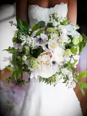 A bride holds an overflowing bouquet of peonies, anemones and greenery.