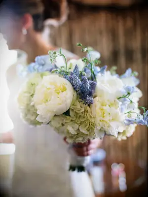 A bride holds a vibrant springtime bouquet in shades of white and blue.