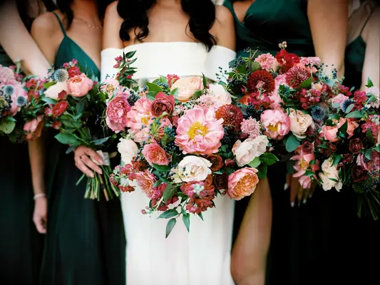 A bride and her bridesmaids hold jewel-toned peony bouquets.