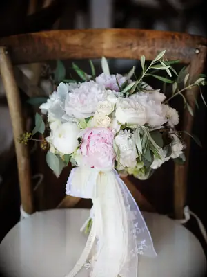 A wooden chair holds a lacy bouquet of white and pale pink peonies.