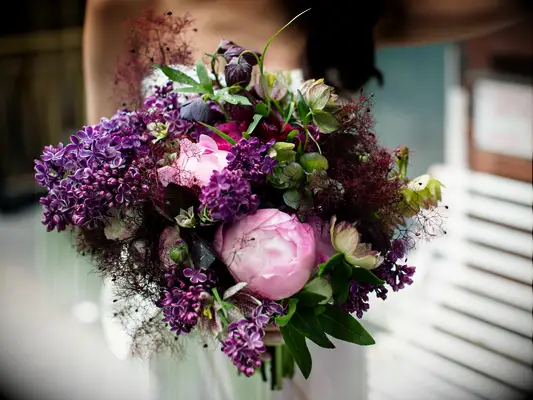 A bride holds a vibrant peony bouquet in shades of pink and purple.
