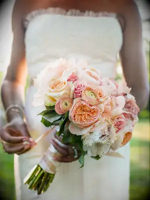 A bride holds a springtime bouquet of peonies in shades of peach and white.