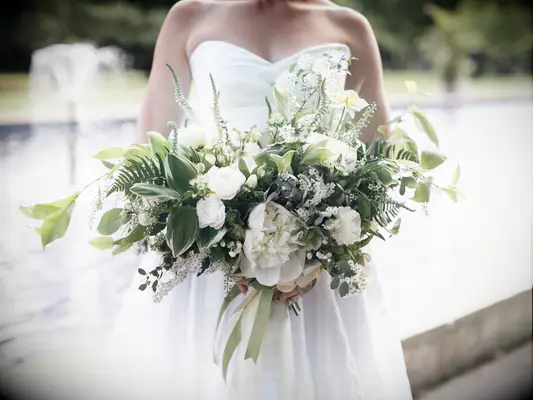 A bride holds an overflowing bouquet of greenery and white flowers.