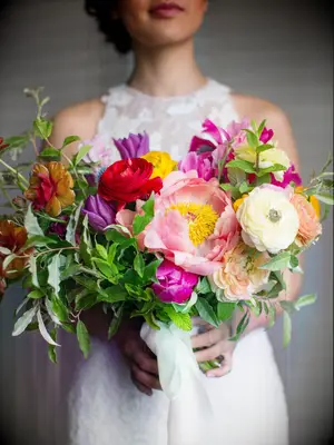 A bride holds a colorful bouquet in riotous shades of red, yellow, pink and purple.