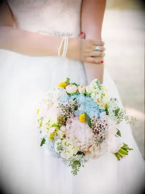 A bride holds a bouquet of pale springtime flowers.