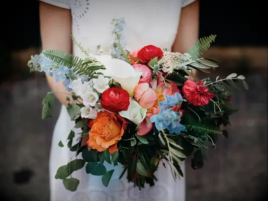 A bride holds a stunning bouquet in shades of red, orange, white and pale blue.