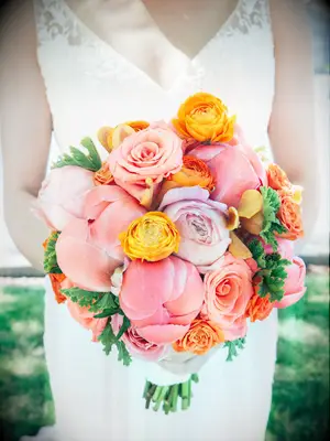 A bride holds a bouquet of vibrant orange and peachy peonies.