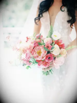 A bride holds a peony and anemone bouquet in ombré shades of pink.