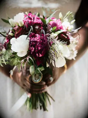 A bride holds a breathtaking bouquet of wine-deep peonies and white petals.