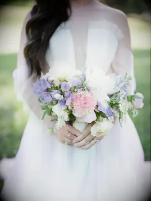 A bride holds a lavender, pink, and white peony bouquet.