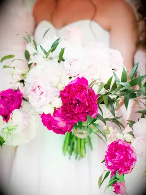 A bride holds an overflowing bouquet of hot pink and white peonies.