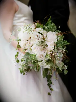A bride holds an overflowing white peony and rose bouqet.
