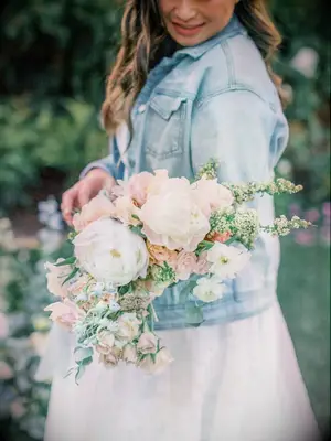 A bride holds a boho-chic bouquet of roses and peonies in pale spring colors.