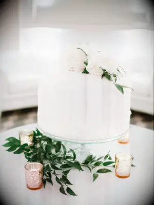 one tier wedding cake with white buttercream frosting and white peonies next to votive candles