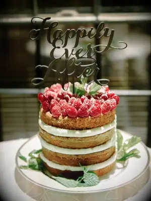 naked one tier wedding cake decorated with raspberries and happily ever after cake topper