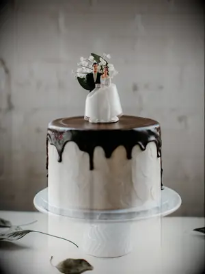 one tier wedding cake with white buttercream frosting, chocolate drip icing and vintage bride and groom topper