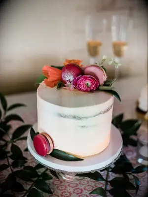 one tier wedding cake with orange ombre frosting, pink and orange flowers and pink macarons