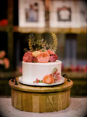 one tier wedding cake on wooden stand with orange, yellow and pink flowers and gold best day ever topper