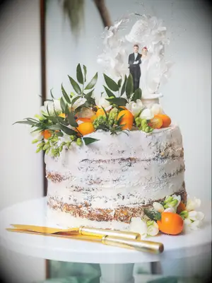 one tier wedding cake with semi-naked frosting, orange kumquats and white freesias with vintage bride and groom cake topper