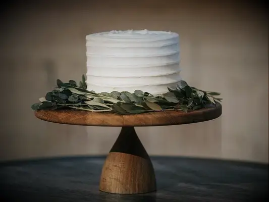 simple one tier wedding cake with white buttercream frosting and boxwood greenery on wooden cake stand
