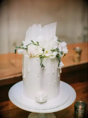 modern one tier wedding cake with fondant, white drip icing, white macarons, white meringue, white flowers and white chocolate pieces