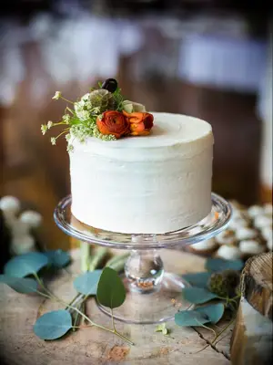 one tier wedding cake with buttercream frosting, red and orange ranunculus, and greenery 