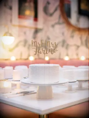 white one tier wedding cake with white sprinkles and gold calligraphy cake topper that says mr. & mrs. farino