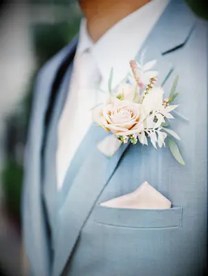 close up of pastel wedding boutonniere with pink rose and bleached greenery on light blue suit jacket