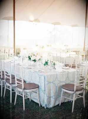 tented wedding reception featuring rectangular table decorated with pastel blue patterned tablecloth and white chiavari chairs