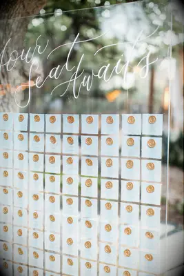 wedding escort card display with pastel blue cards and gold wax seals on clear acrylic board 
