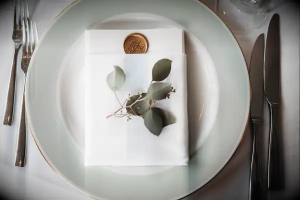 wedding place setting with sage green dinner plate, white menu card folded into napkin and sprig of fresh eucalyptus