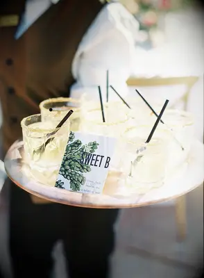 server holding a tray of light yellow colored drinks with black straws