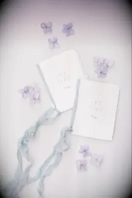 styled flat lay with handmade wedding vow books decorated with light blue silk ribbons, calligraphy and purple hydrangea petals