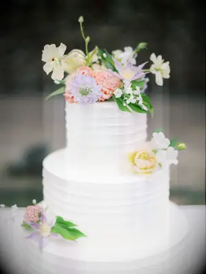 three tier white buttercream wedding cake decorated with pastel purple, yellow and coral flowers